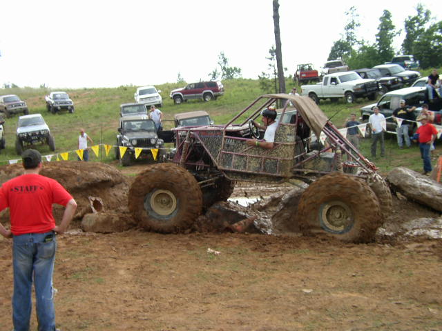 Custom buggy with large tires stuck in mud, spectators watch