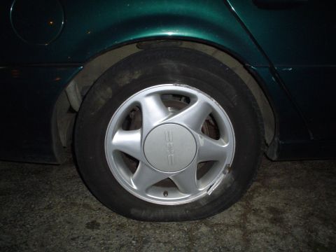 1993 Ford Taurus - Rear wheel and fender of a dark green car, showing a silver hubcap.