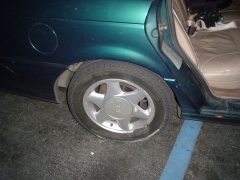 1993 Ford Taurus - The rear passenger side of a car is shown, with a flat tire and an open door revealing the interior.