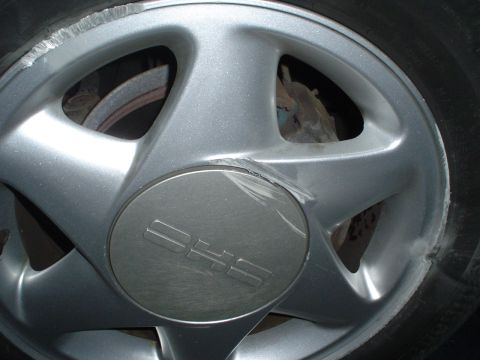 1993 Ford Taurus - Close-up of a silver wheel with a "DHS" logo on the center cap, showing signs of curb rash.