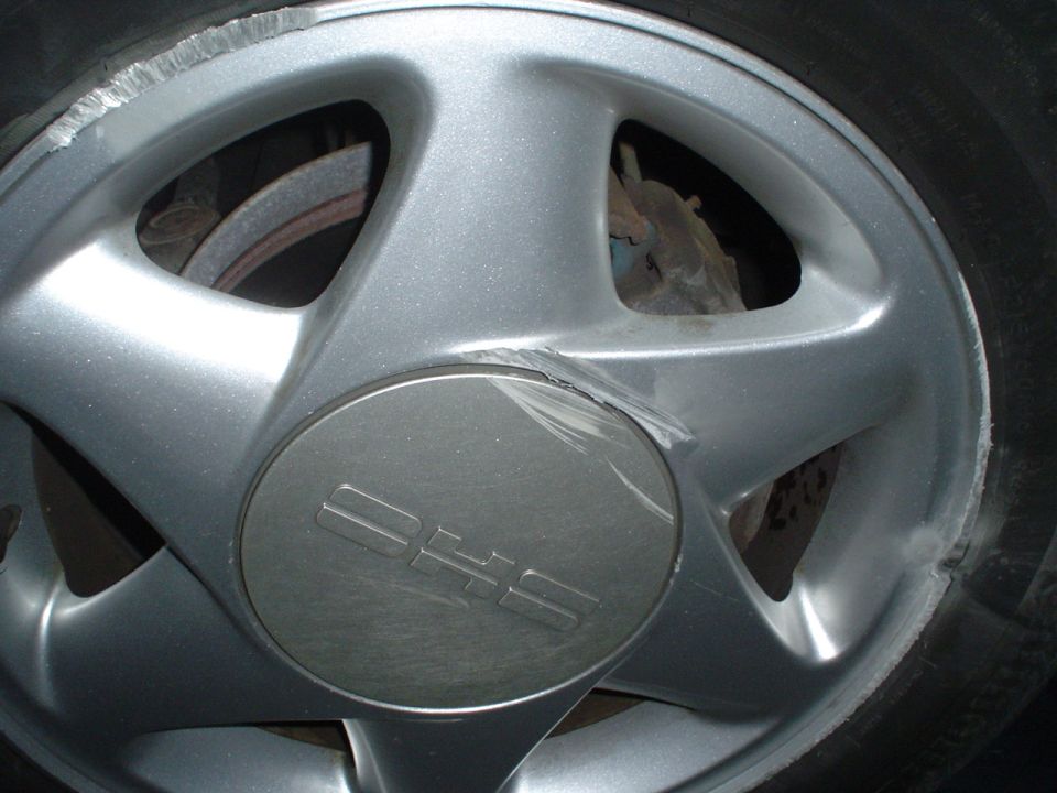 Silver wheel with "DHS" center cap and curb rash