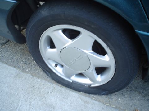 1993 Ford Taurus - A car with a flat tire is pictured, showing the wheel and the deflated tire resting on the rim.