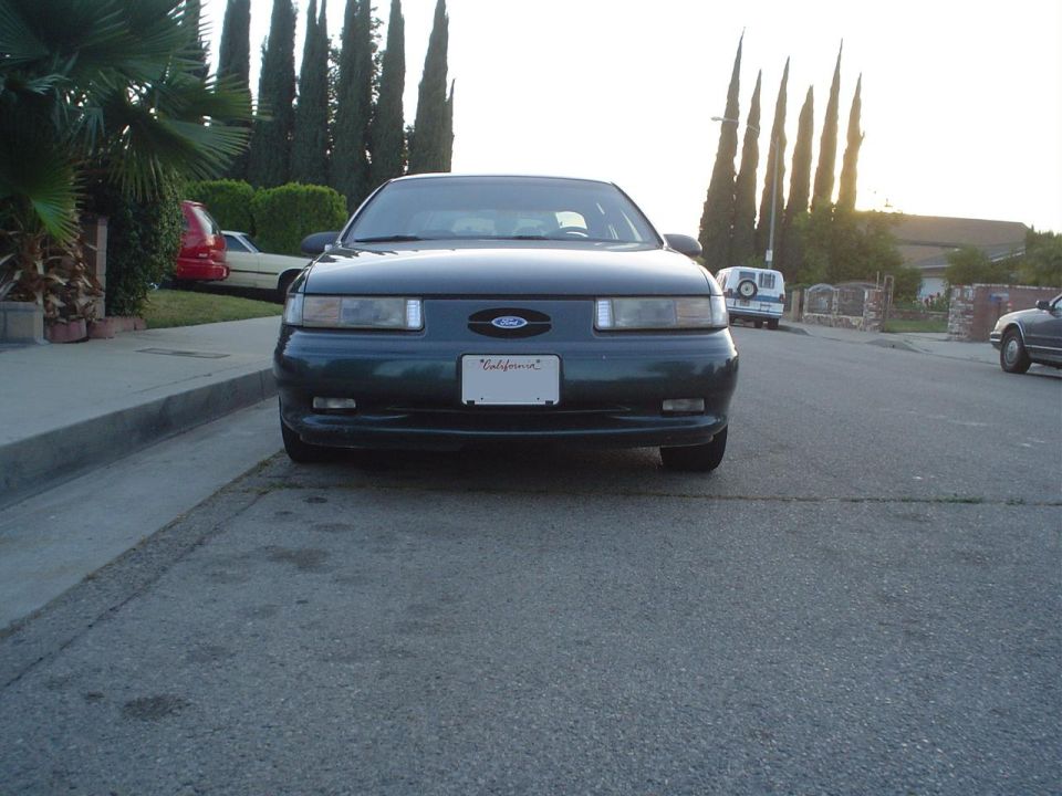Dark green Ford Taurus parked on street, front view. California license plate visible