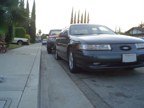 1993 Ford Taurus - A 1993 Ford Taurus is parked curbside on a sunny day, with other vehicles visible in the background.