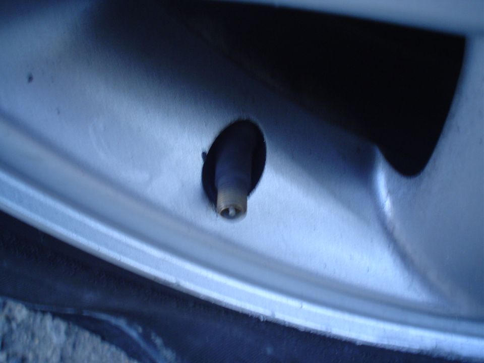 Close-up of a tire valve stem protruding from a silver alloy wheel