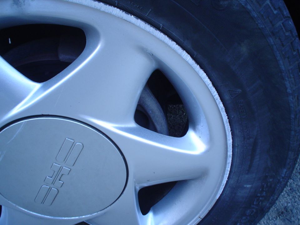 Close-up of a silver alloy wheel with a tire. The wheel has a center cap with an embossed logo