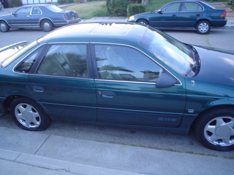 1993 Ford Taurus - Side profile of a green 1993 Ford Taurus sedan, a sunroof and parked on a residential street.