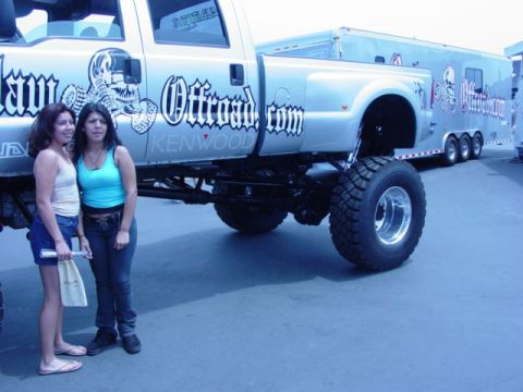 1992 Ford Bronco - A silver lifted pickup truck with custom graphics is parked next to a trailer, with two women standing nearby.