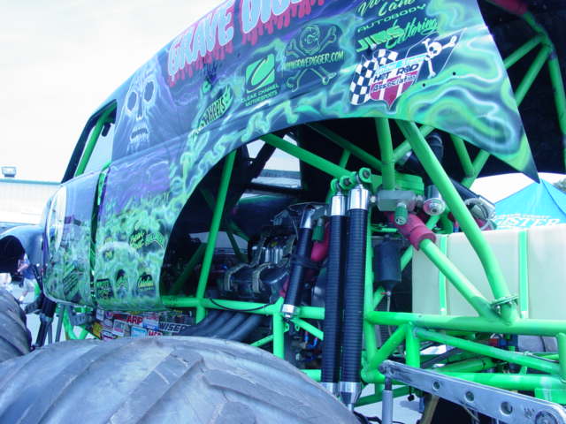 Monster truck with green and purple flame graphics, showing engine and suspension components