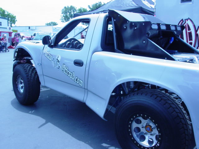 White custom pickup truck with "Outlaw Offroad.com" decal on door and a large rear spoiler with lights