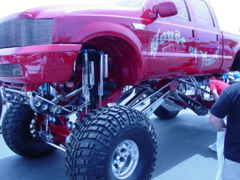 1992 Ford Bronco - A heavily modified red pickup truck with custom graphics and an extreme lift kit is on display.