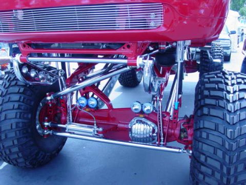 1992 Ford Bronco - A heavily modified red truck with oversized tires and a custom suspension system is displayed at an off-road show.