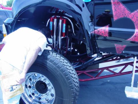 1992 Ford Bronco - A person examines the custom suspension and large tire of a modified off-road vehicle.
