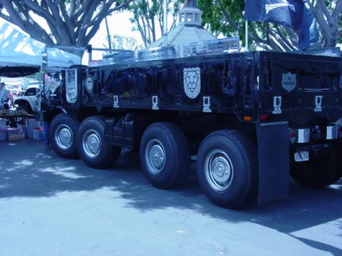 1992 Ford Bronco - A large black dump truck with several axles is parked outdoors under trees.