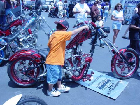 1992 Ford Bronco - A custom chopper motorcycle is displayed at an event, with a child looking on. The sign indicates it's a 'Double 280 Softail Chopper'.