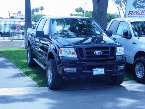 1992 Ford Bronco - A black Ford F-150 truck is parked at an outdoor event, with a white Ford truck visible to its right.