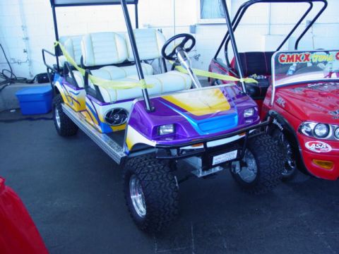 1992 Ford Bronco - Customized golf carts are displayed at an event, with a red cart next to a purple and yellow one.