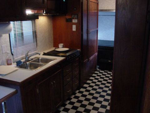 1992 Ford Bronco - Interior view of an RV kitchen area with a sink, stove, and wood cabinetry, leading to a bedroom.