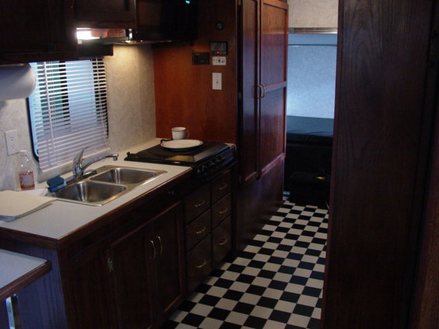 RV interior showing a sink, stove, cabinets, and a checkered floor leading to a bedroom area