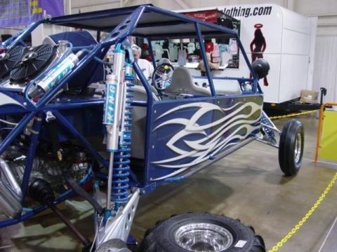 1992 Ford Bronco - A custom blue dune buggy with flame graphics is displayed indoors, with a trailer and merchandise visible behind it.