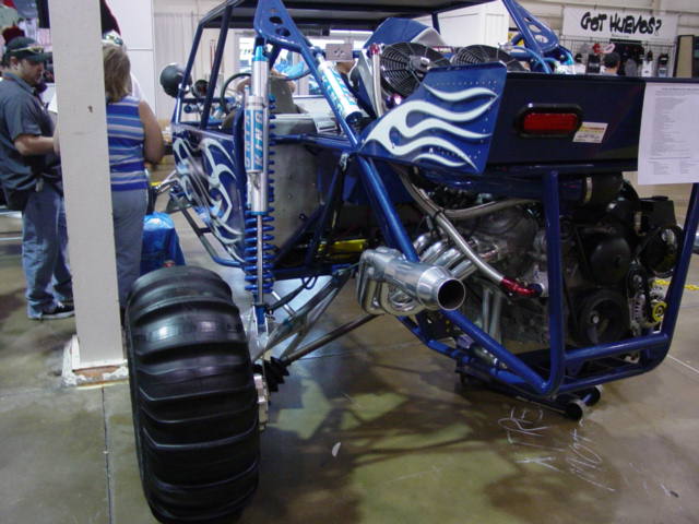 Custom dune buggy with blue frame, flame decals, large rear paddle tire, and exposed V8 engine