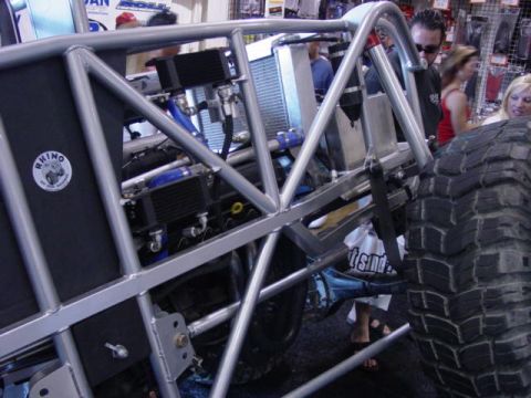 1992 Ford Bronco - Close-up of a custom off-road vehicle's exposed chassis and large tire at an indoor event.