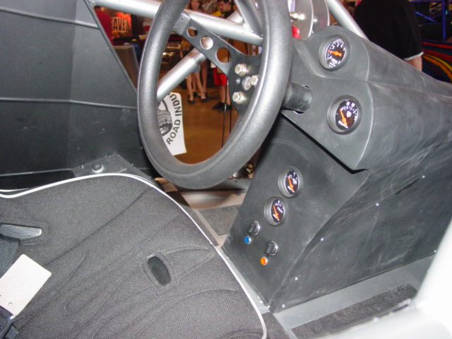 Interior shot of a race car with a steering wheel, dashboard gauges, and racing seat