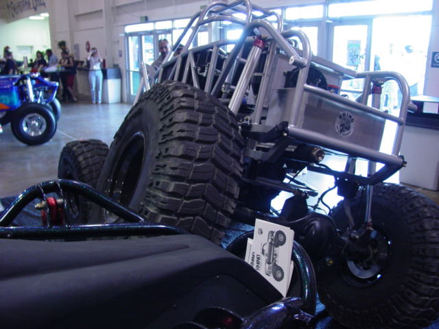 Off-road buggy rear suspension and massive tire, with a blue ATV in the background
