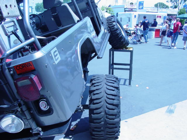 Jeep Wrangler lifted with big tires, one on a stand. People and food trucks in background