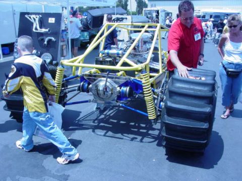 1992 Ford Bronco - A custom off-road vehicle with oversized paddle tires and a prominent yellow roll cage is displayed at an outdoor event.