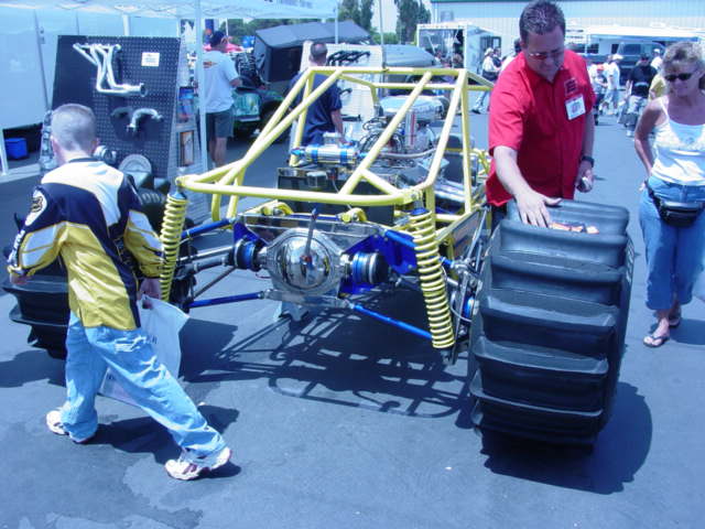 Custom off-road vehicle with large paddle tires and yellow roll cage, viewed from the rear