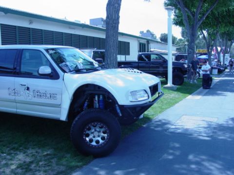 1992 Ford Bronco - Modified white SUV with custom off-road suspension and tires, parked outdoors with other vehicles and people.