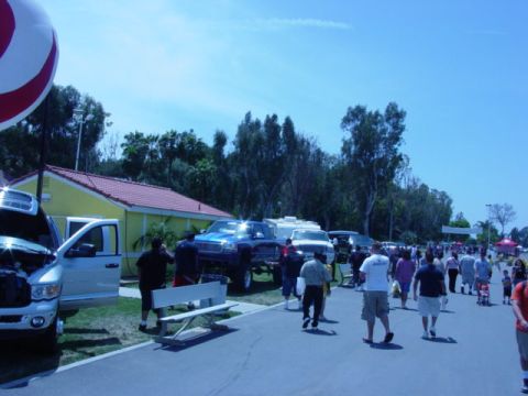 1992 Ford Bronco - An outdoor event with several trucks and trailers on display, with attendees milling about under a clear blue sky.