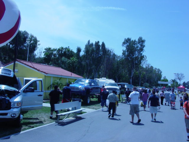 people walking around trucks and trailers outside a yellow building, big red and white balloon overhead