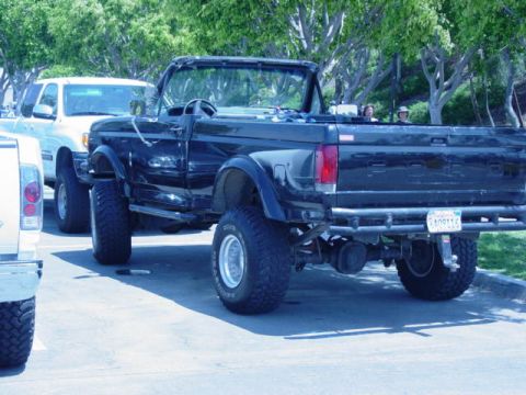 1992 Ford Bronco - A black 1992 Ford Bronco convertible is parked next to another vehicle, modified for off-road use.