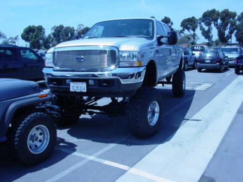 1992 Ford Bronco - A lifted silver Ford F-250 Super Duty truck is parked in a lot, dwarfing a nearby Jeep.