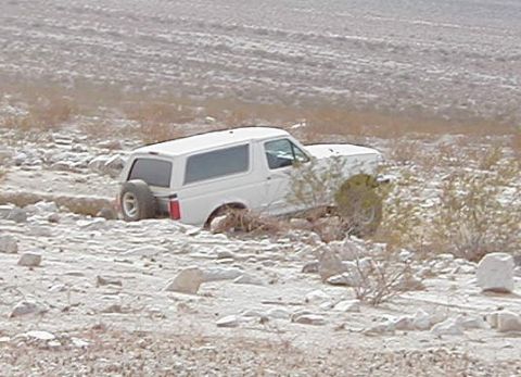1993 Ford Bronco - A white 1993 Ford Bronco is partially submerged in a rocky ditch in a desert environment.