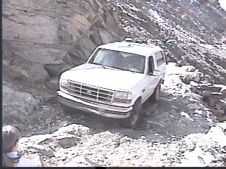 1993 Ford Bronco - A white 1993 Ford Bronco navigates a challenging rocky terrain, its grille clearly visible.