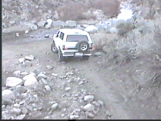 1993 Ford Bronco - A white 1993 Ford Bronco navigates a rough, rocky terrain on a trail.