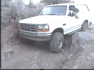 1993 Ford Bronco - White 1993 Ford Bronco driving over rocks on a trail.