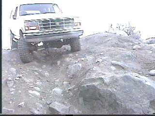 1993 Ford Bronco - A white SUV navigates a challenging rocky terrain, with the SuperMotors logo in the corner.