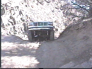 1993 Ford Bronco - A white Ford Bronco navigates a narrow dirt path surrounded by steep, rocky terrain.