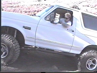 1993 Ford Bronco - A white 1993 Ford Bronco is shown from the driver's side, 3/4 front view, with a man at the wheel.