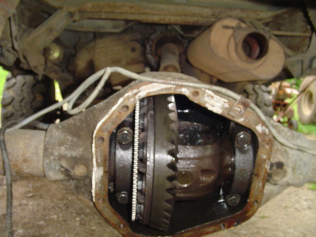 Open rear differential with carrier and ring gear exposed underneath a vehicle outdoors