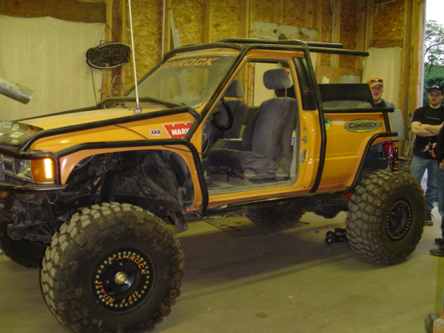 Modified Toyota pickup truck with large off-road tires and roll cage, doors removed