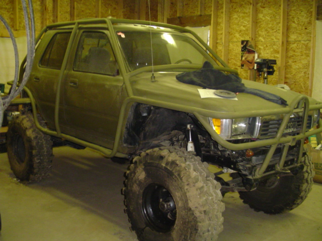 Olive green Toyota 4Runner with a roll cage and large off-road tires, parked inside a garage