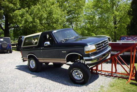 1995 Ford Bronco - A lifted 1995 Ford Bronco with tan trim is parked outdoors, with other vehicles visible in the background.