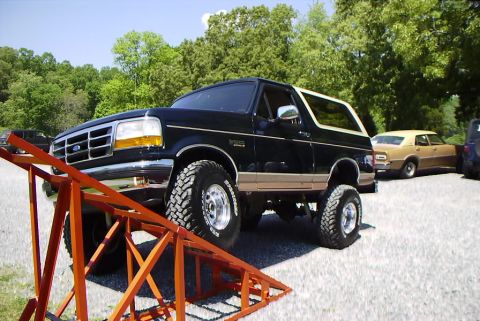1995 Ford Bronco - Black 1995 Ford Bronco with tan trim is positioned on an orange ramp, with other vehicles in the background.