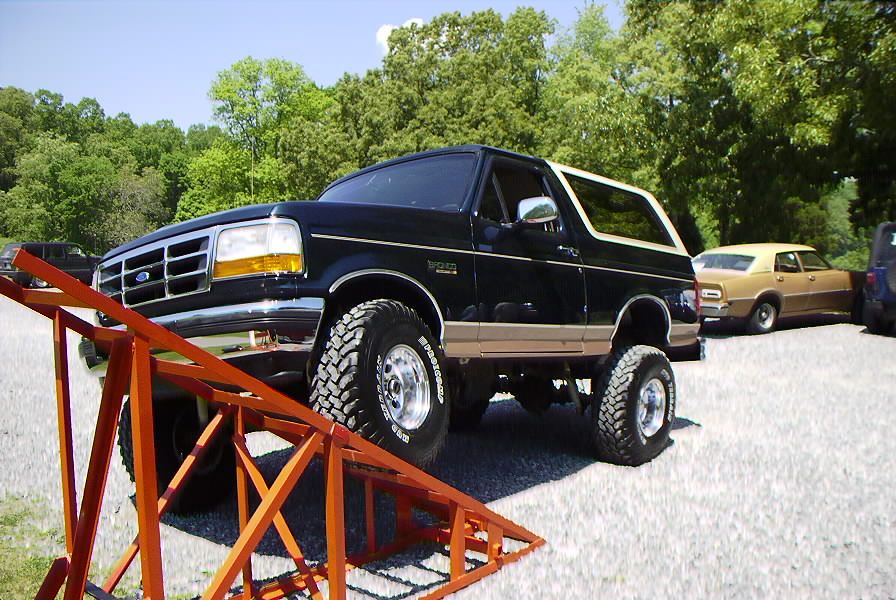 Black 1995 Ford Bronco with tan trim on an orange ramp, other vehicles parked behind