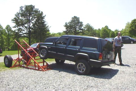 1995 Ford Bronco - A man stands next to a Jeep Cherokee XJ that is partially on an orange metal ramp structure.